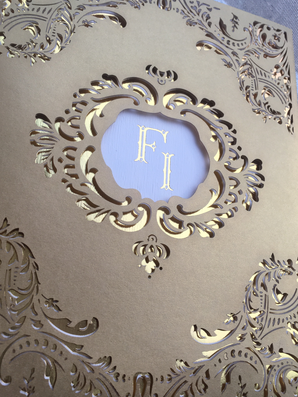 Ornate laser-cut invitation in metallic gold with intricate filigree framing a monogram, a bold custom wedding invitation design that feels regal, detailed, and highly decorative.