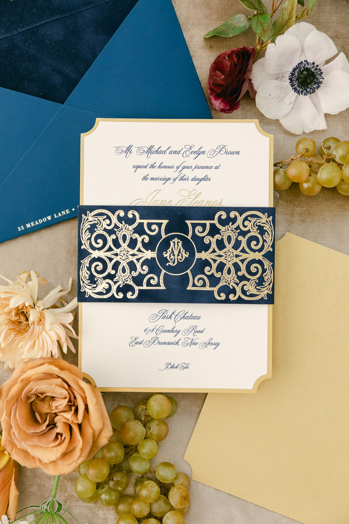 Classic navy and gold invitation with ornate laser-cut belly band, styled with florals and grapes, a refined custom wedding invitation design with formal, European-inspired details.