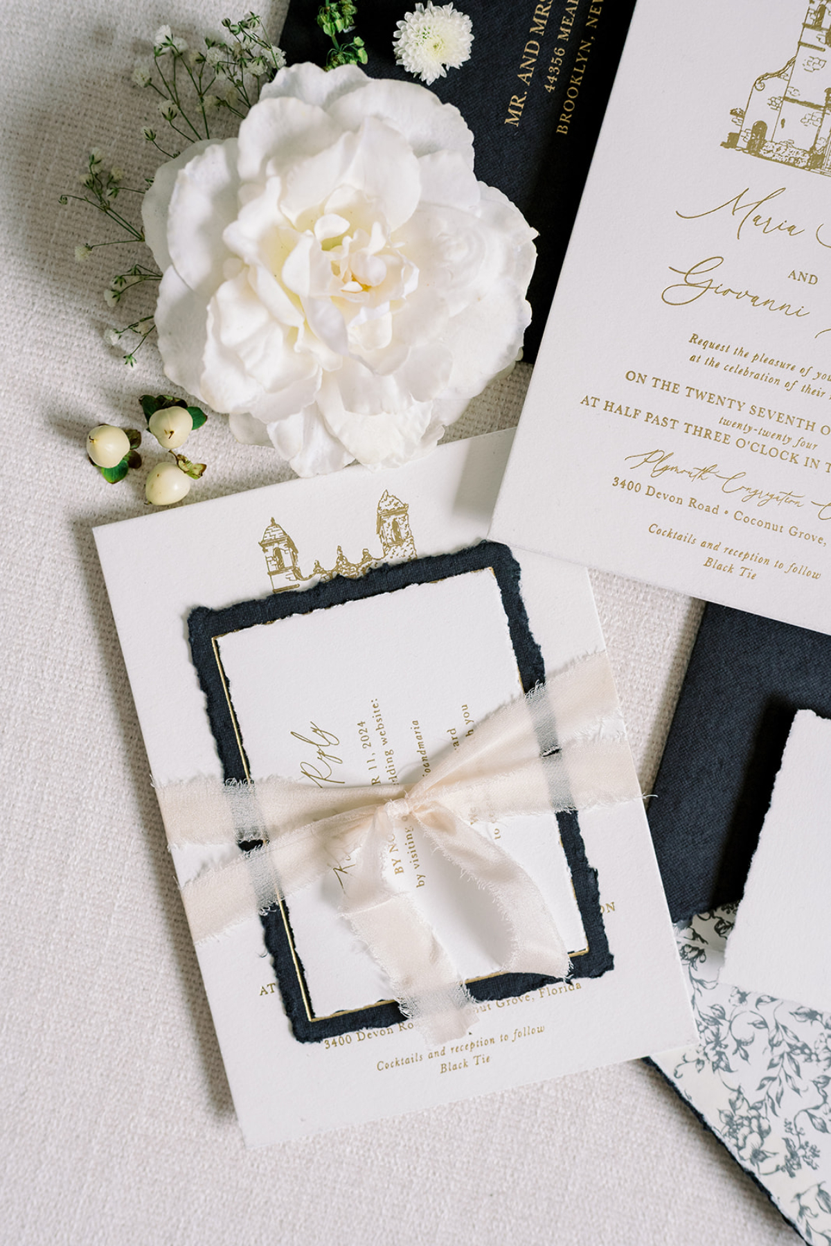 Romantic black, white, and gold invitation suite with deckled edges, silk ribbon, and soft florals, a custom wedding invitation design blending texture, softness, and timeless elegance.