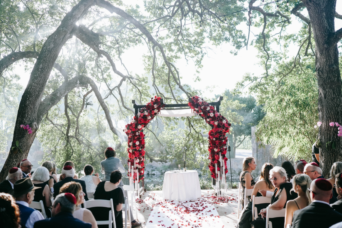 Outdoor ceremony with guests seated around a floral arch overlooking water and trees, capturing a serene and intimate moment during a destination wedding in Florida.