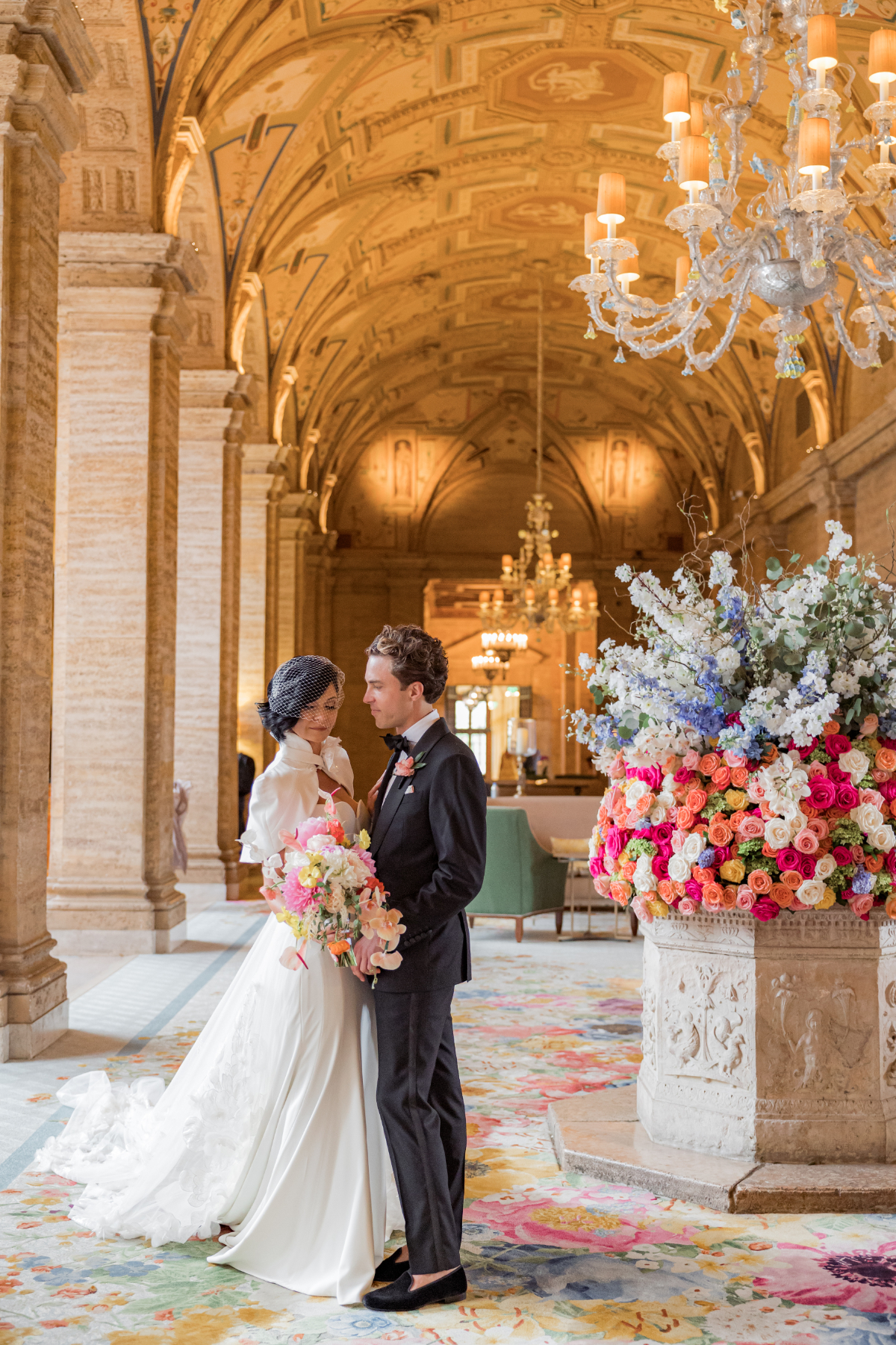 Couple standing inside a grand ballroom with ornate ceilings, chandeliers, and vibrant floral arrangements, capturing the opulence of an indoor destination wedding in Florida venue.